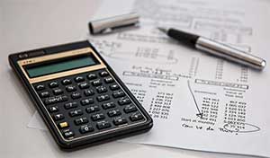 Zoomed-in shot of a calculator and pen resting on a company’s expenses spreadsheet